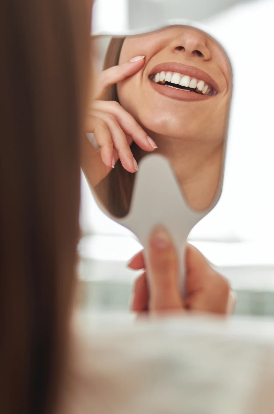 Fotografía de una mujer mirando su sonrisa en un espejo de mano
