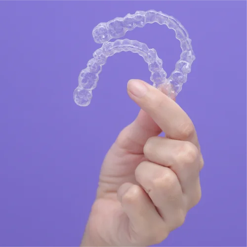 Fotografía de una mano sujetando unos alineadores Invisalign con fondo morado